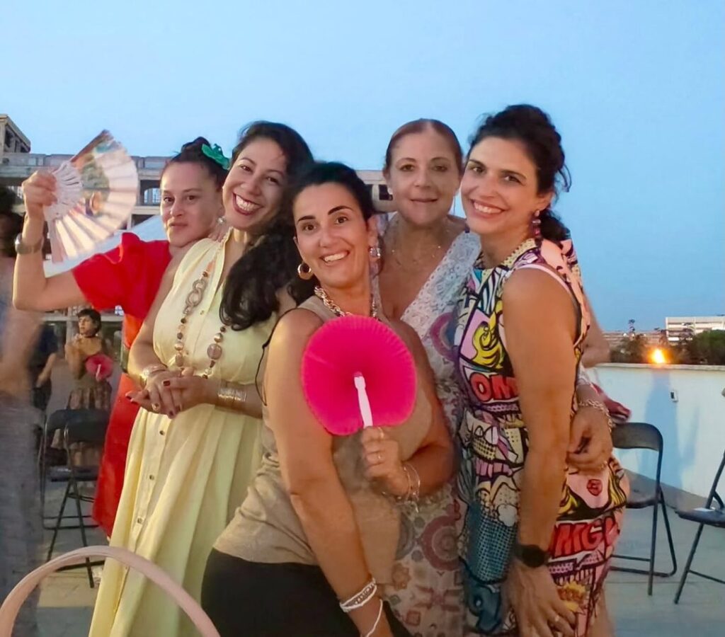 Cinque donne sorridenti con i ventagli al tramonto sulla terrazza di Dress for Success Rome