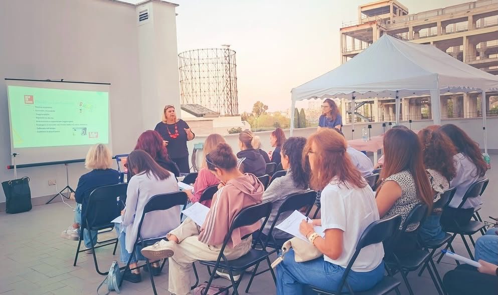 La relatrice davanti allo schermo e le partecipanti sulla terrazza di Dress for Success Rome, con il Gazometro sullo sfondo
